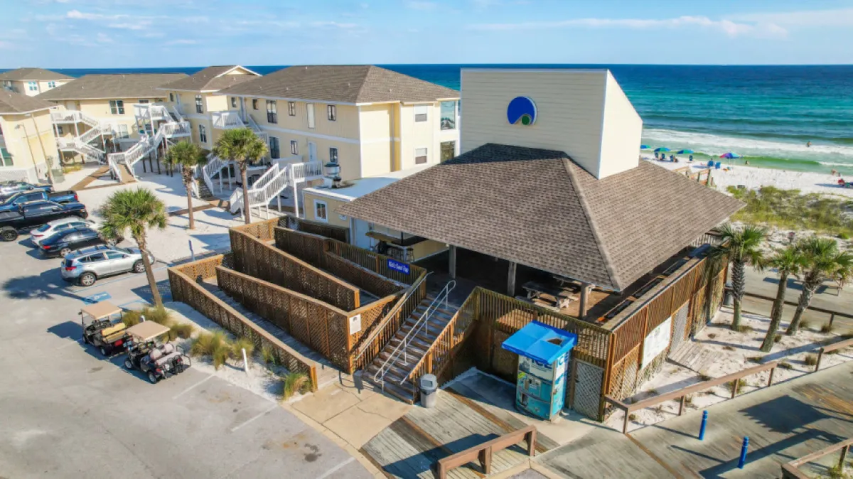 A beachfront property with palm trees, a boardwalk leading toward the sand, and visible outdoor spaces ideal for gathering or relaxing. The scene radiates a laid-back, welcoming vibe.