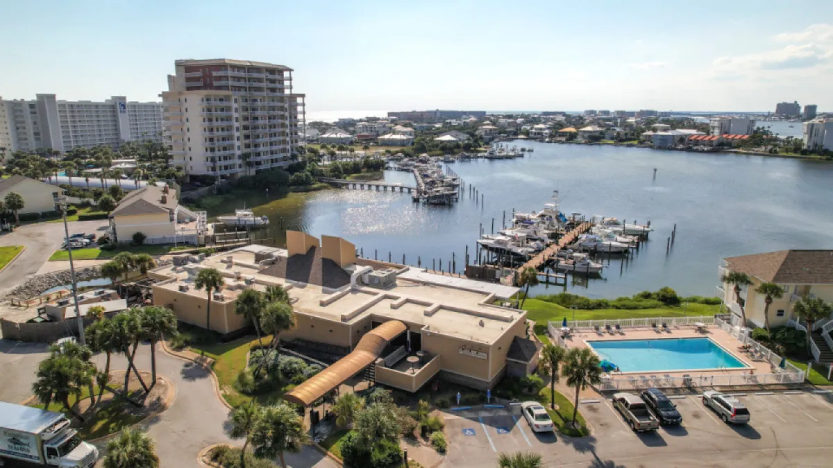 This image showcases a resort-style swimming pool overlooking a marina, with boats docked nearby and lush landscaping. The setting is lively yet relaxed, offering ample space for guests to lounge poolside or gather for social events as the sun sets over the water.