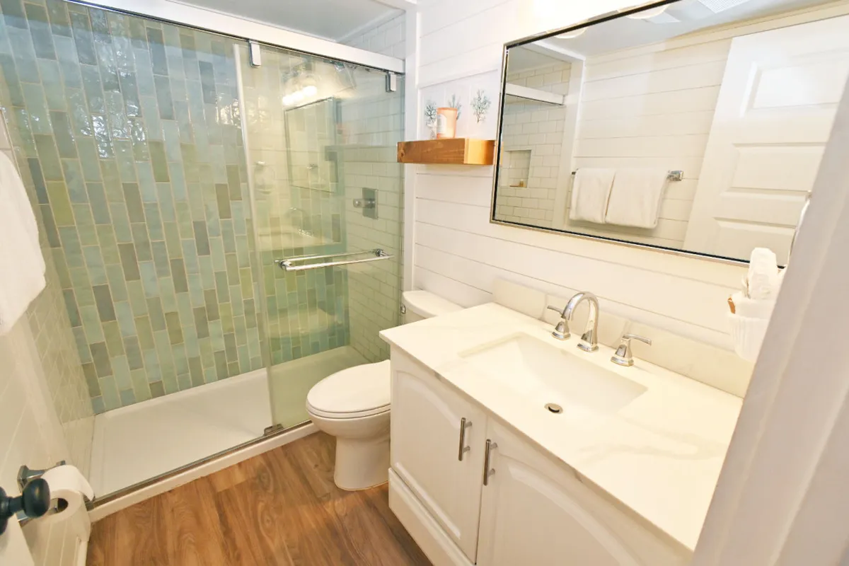 A spa-inspired bathroom featuring a sleek glass shower enclosure, a modern vanity with a sink, a large mirror, and decorative shelving. The setting is serene and thoughtfully designed, inviting relaxation and self-care.