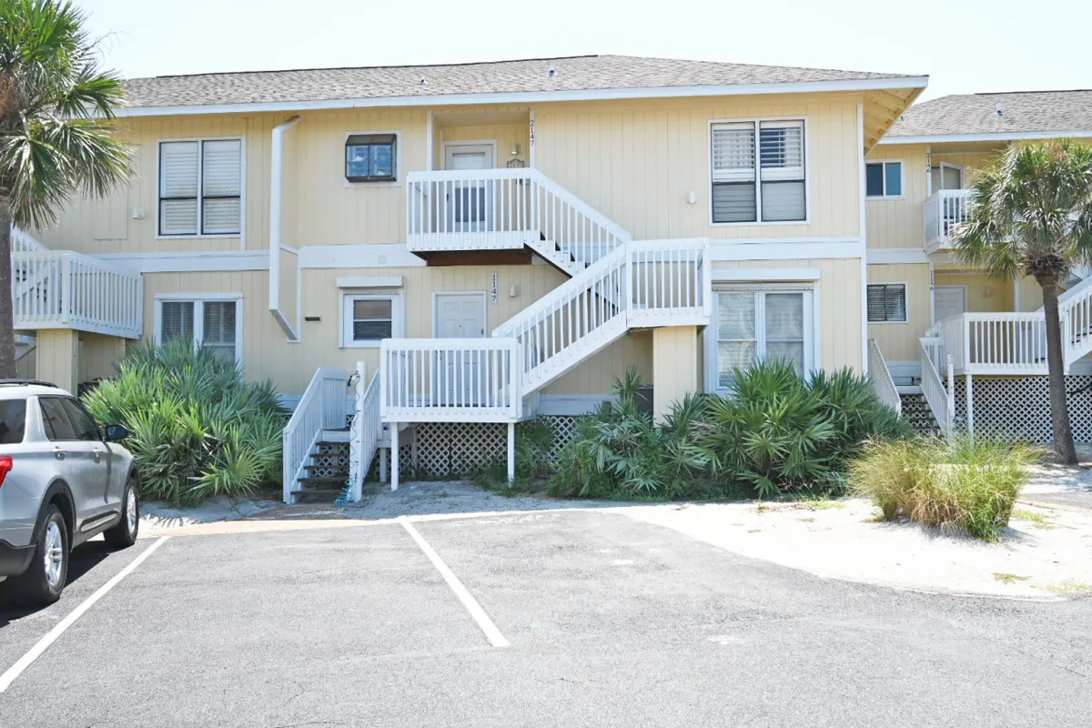An inviting exterior shot featuring staircases, palm trees, and home entrances, with outdoor seating areas hinted at beneath the shade. The relaxed, casual atmosphere suggests spaces to enjoy coffee breaks or casual work sessions outdoors.