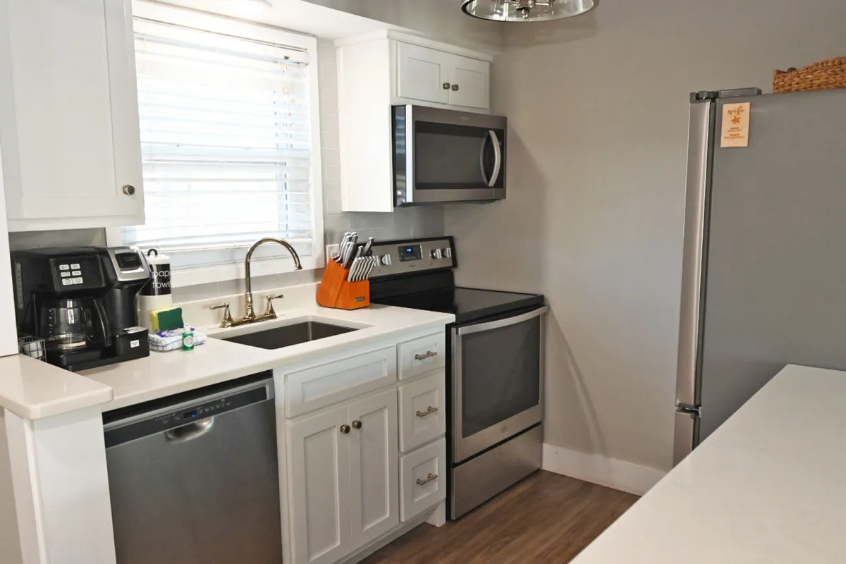 A welcoming kitchen scene anchored by gleaming stainless steel appliances, white cabinetry, and generous countertop space, all bathed in natural light. The setup highlights the room’s functionality for cooking, entertaining, and family gatherings.