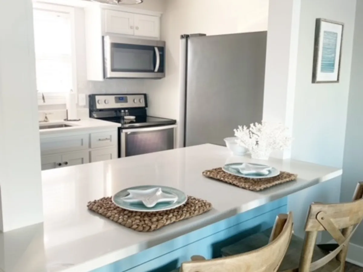 This image spotlights a bright, modern kitchen featuring a central island with starfish-themed table settings, sleek appliances, and a spacious layout perfect for culinary activities or casual dining. The area is cheerful and inviting, ideal for both gourmet cooking and everyday meals.